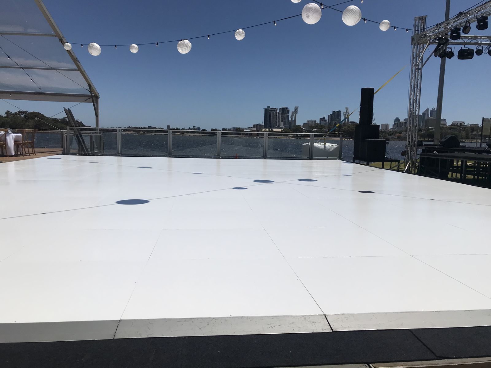 Large white dance floor under festoon lights at an open-air riverside event