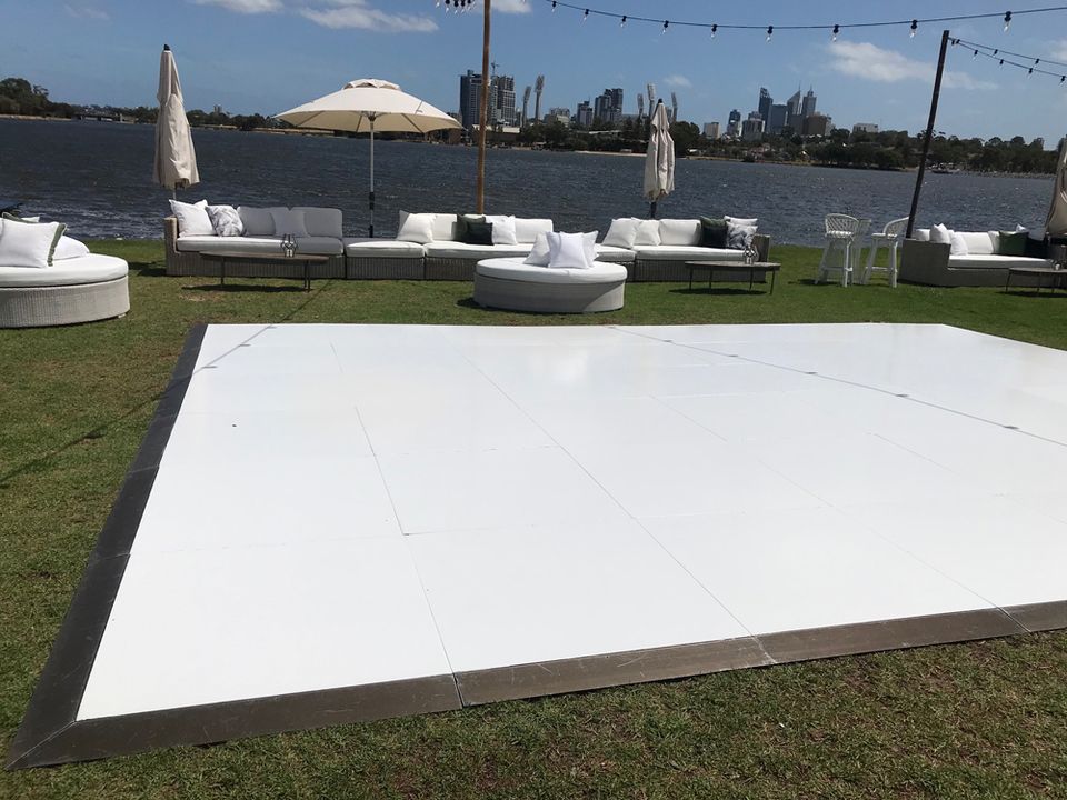 White gloss dance floor set up on a riverside lawn with lounge seating and the Perth skyline behind