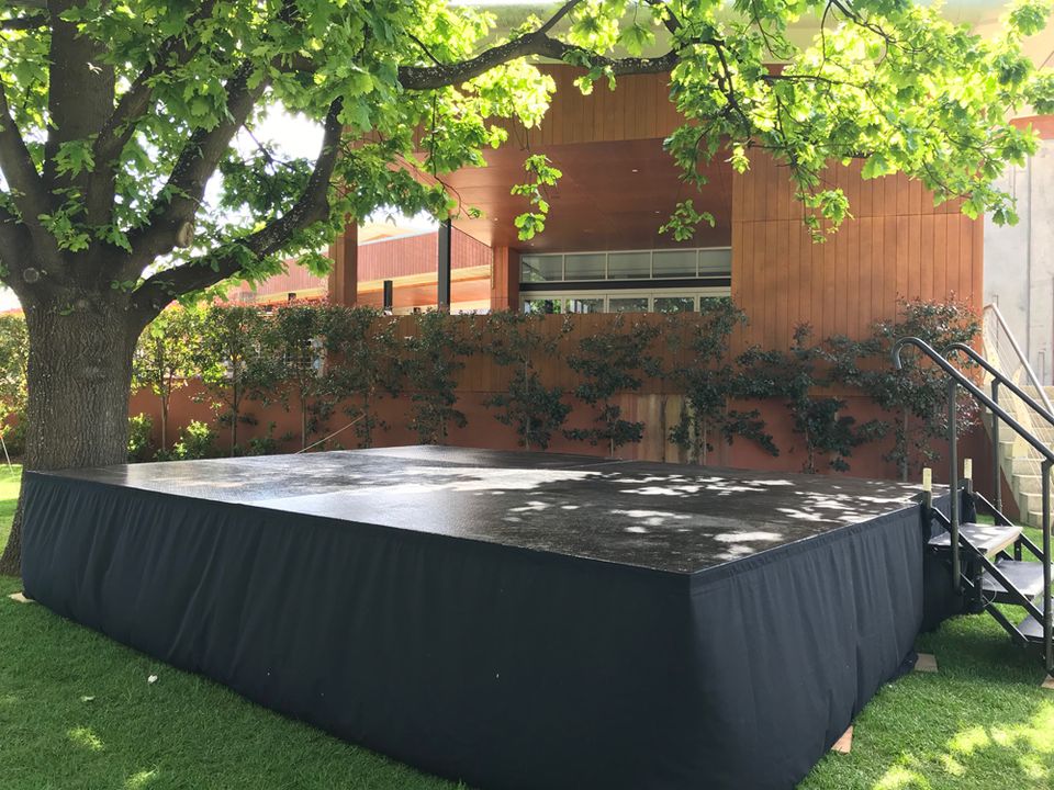 Black skirted stage under a tree in a garden